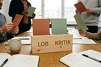 Auf einem Tisch stehen Kärtchen mit der Überschrift Lob und Kritik.