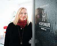 Eine blonde Frau steht an einer Tür mit der Aufschrift Hospizhilfe Bremen.