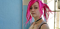 Junge Frau mit bunten / pinken Haaren, Piercings usw. guckt in die Kamera.