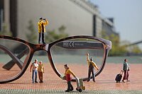 Miniaturfiguren, die ihrer Arbeit nachgehen und sich um eine Brille versammeln.