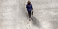 Vogelperspektive auf eine Frau, die über einen graune Untergrund läuft