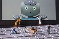 Diverse Miniaturfiguren, die auf einer Tastatur laufen und vor einem Tablet sich befinden, dass einen Roboter zeigt.