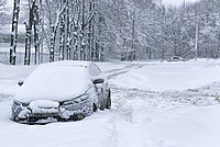 Verschneite Straße sowie ein verschneites Auto