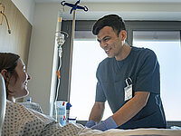 Aref Azizi steht am Bett einer Patientin im St. Josef-Stift und lächelt sie an