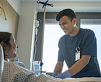 Aref Azizi steht am Bett einer Patientin im St. Josef-Stift und lächelt sie an