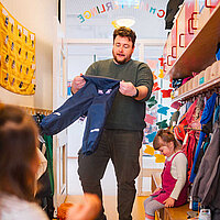 Erzieher in einer Kita, der beim Anziehen einer Regenhose hilft.