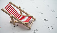 Urlaubsplanung Liegestuhl Ein Mini-Liegestuhl steht auf einem Kalenderblatt