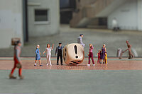 Diverse Miniaturfiguren, die sich um einen Würfel mit einem Ausrufezeichen versammeln