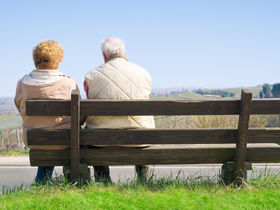 Zwei Senioren sitzen auf Holzbank und blicken in die Ferne.