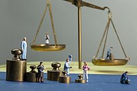 Diverse Miniaturfiguren, die sich vor dem Symbol der Justitia (Waage) stehen.