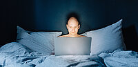 Ein Mann sitzt nachts im Bett mit seinem Laptop