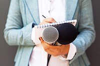Person hält zwei Mikrofone, einen Notizblock und einen Stift – Symbolbild für Pressearbeit und Medienanfragen.