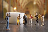 Miniaturfiguren in einer Kirche, im Hintergrund ein Teelicht.