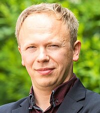 René Böhme Ein Porträtfoto von René Böhme vor einer grünen Hecke