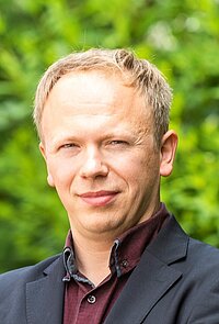Ein Porträtfoto von René Böhme vor einer grünen Hecke