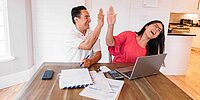 Ein lachendes Pärchen am Schreibtisch, die sich eine High-Five geben. Vor ihnen liegen diverse Steuerunterlagen.
