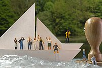 Diverse Miniaturfiguren, die auf einem Boot sind und sich auf dem Weg zu einem Stempel befinden.