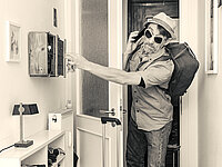 Ein Mann mit Sonnenbrille und Reisegepäck steht in der Tür.