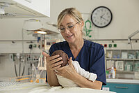 Eine Pflegekraft am St.-Josef-Stift hält den Kopf eines Säuglings mit den Händen