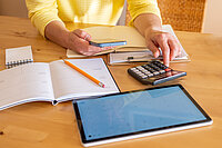 Eine Frau gibt Zahlen in Handy und Taschenrechner ein. 