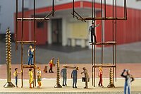 Diverse Miniaturfiguren, die Arbeitskleidung tragen und unter einem Gerüst stehen.