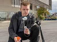 Nils Fricke, Volontär bei Radio Bremen, kniet auf dem Boden, hält ein Smartphone auf einem Gimbal und ein Mikrofon, daneben steht ein Stativ.