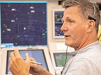 Sven Wilke, Fluglotse in der Radarkontrollzentrale Bremen, spricht während der Arbeit mit Headset vor mehreren Radarschirmen.