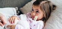 Ein Mädchen liegt mit einem Fieberthermometer im Bett