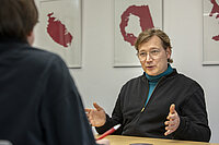 Peer Rosenthal gestikuliert im Interview am Tisch sitzend, im Hintergrund Kunst an der Wand